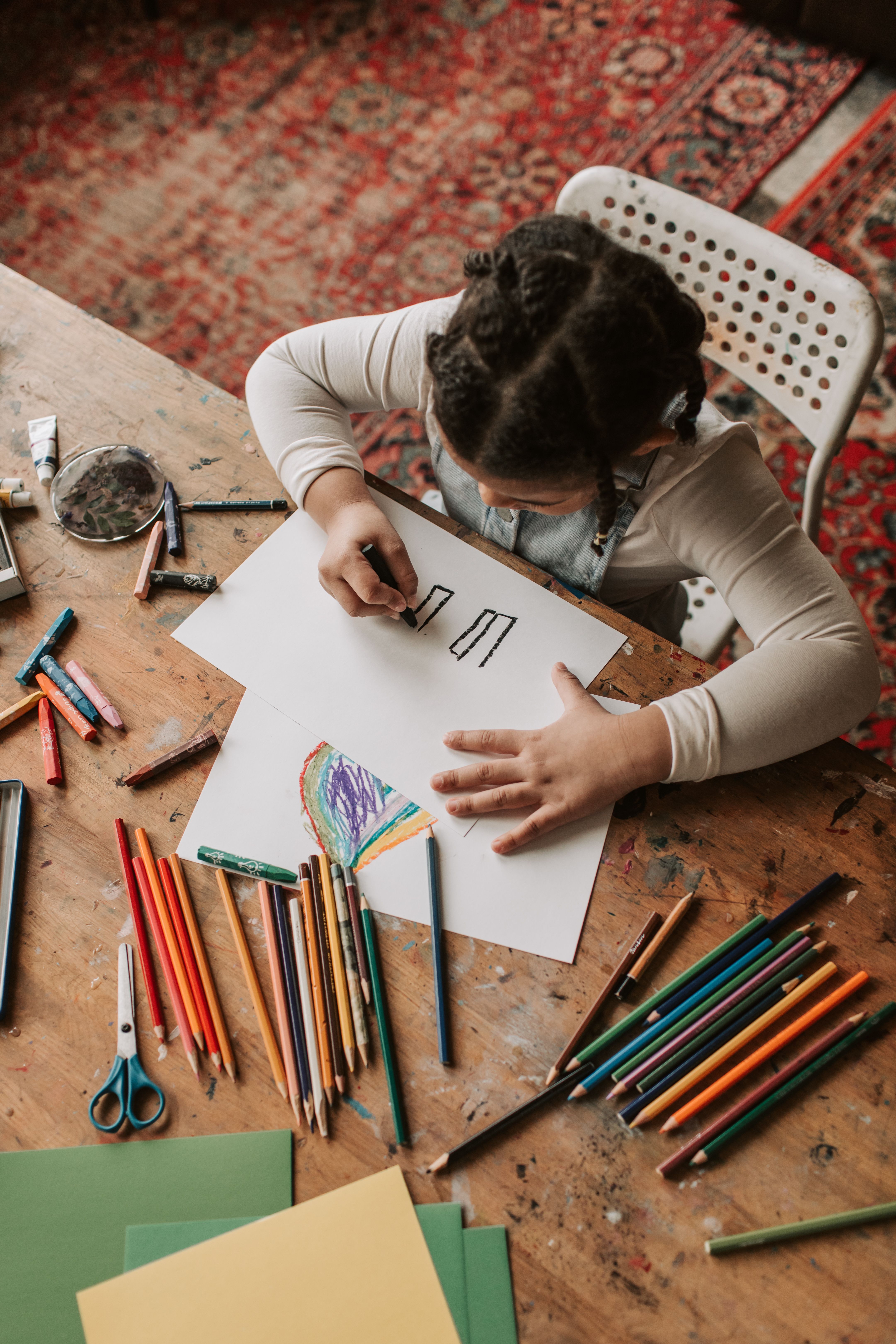 Un.e enfant dessine sur une feuille blanche, il y a beaucoup de crayons autour de lui/elle. Cette image est utilisée pour illustrer la page coloriage.